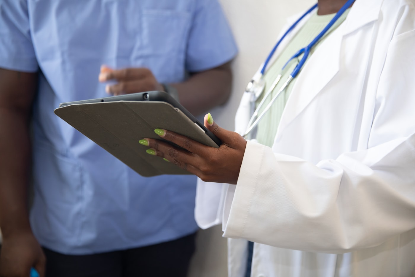 A clinician in a white coat holding a tablet while speaking with a colleague.
